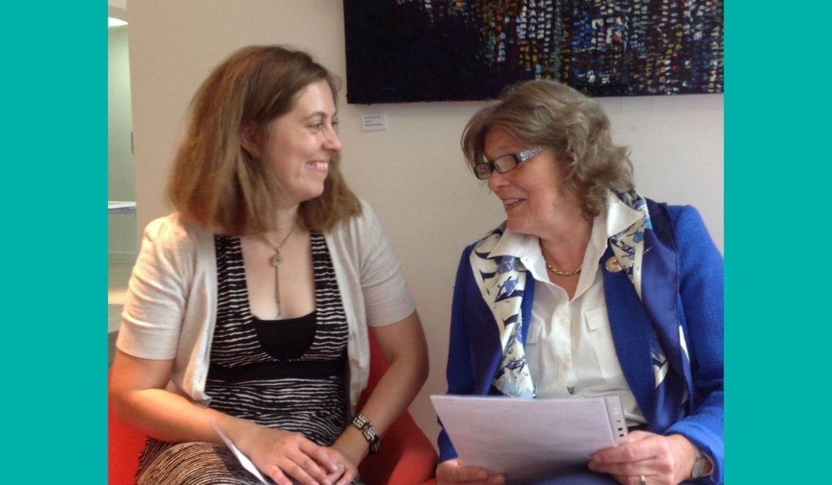 Adele Warner sits to the right on a sofa with Claudia Freeman to the left. They are talking and smiling with one another.